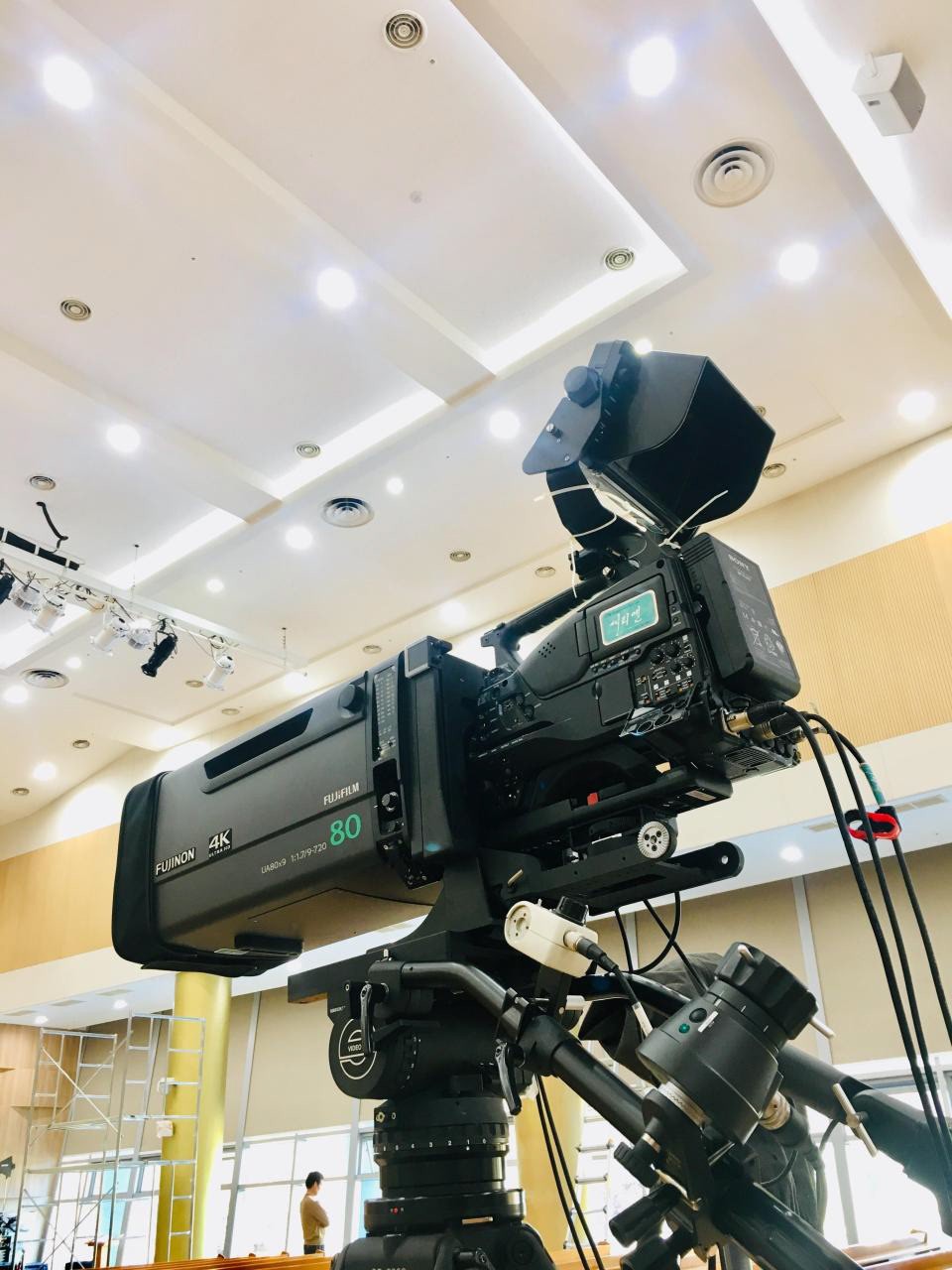 A broadcast camera on a tripod inside a venue